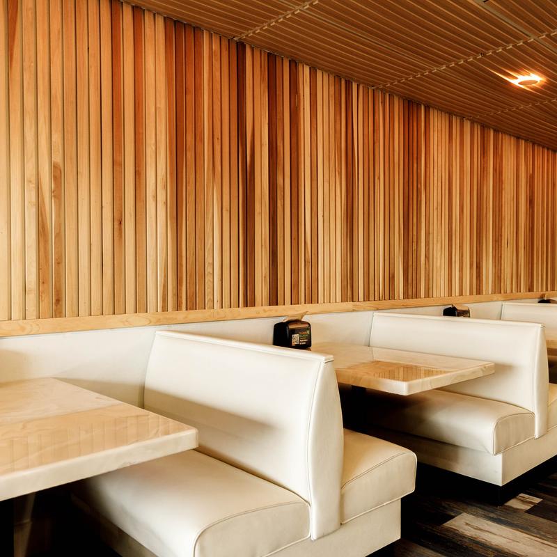 Interior featuring white booths paired with light wood vertical slat wall panels.